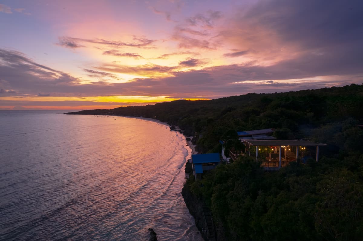Sunset over the sea from above the cliff, the deck lit among the trees