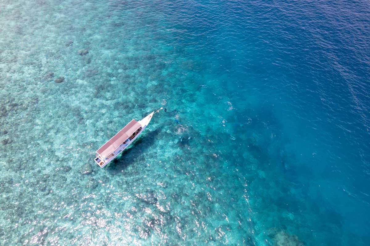 A wooden boat moored over the reef in turquoise water, seen from directly above